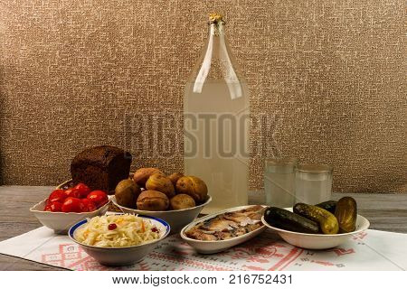 Ukrainian national drink and snack. The big bottle and glass of moonshine on old wooden table. Russian vodka and snack.