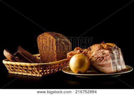 Onion and bekon in the plate and loaf of fresh rye bread with slices isolated on black background.
