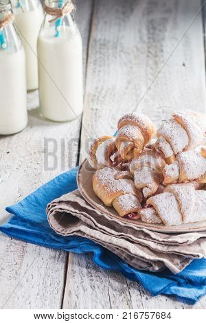 Rugelach with jam filling on plate with milk on wooden background
