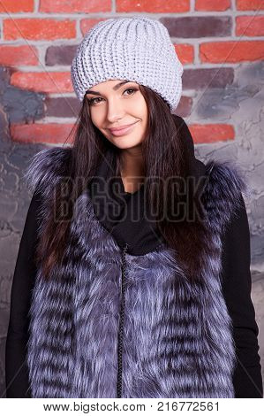 girl in hat and fur coat, against a brick wall background