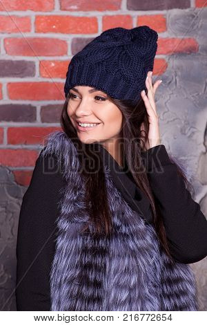 girl in hat and fur coat, against a brick wall background
