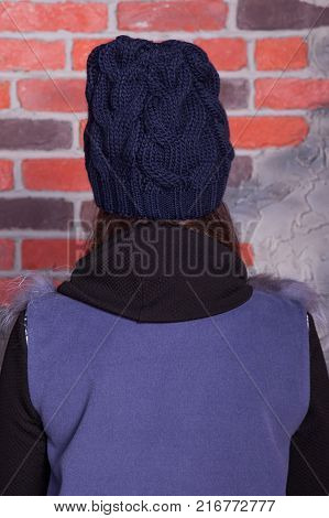 girl in hat and fur coat, against a brick wall background