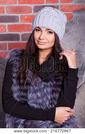 girl in hat and fur coat, against a brick wall background