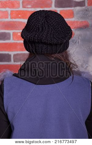girl in hat and fur coat, against a brick wall background