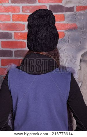 girl in hat and fur coat, against a brick wall background