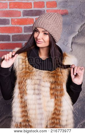 girl in hat and fur coat, against a brick wall background