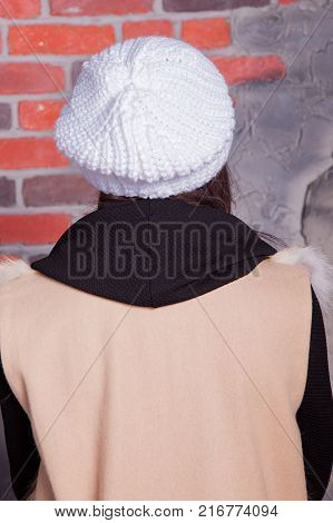 girl in hat and fur coat, against a brick wall background
