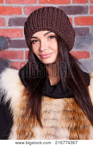 girl in hat and fur coat, against a brick wall background