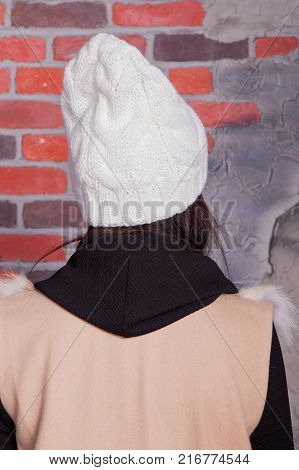 girl in hat and fur coat, against a brick wall background