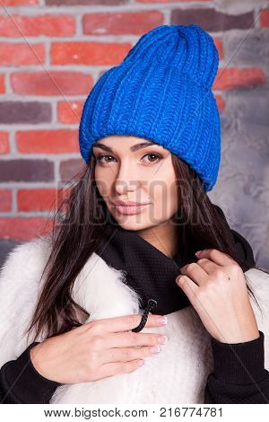 girl in hat and fur coat, against a brick wall background