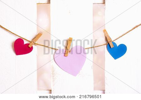 Three paper hearts on a string - Valentine day theme image with one big pink heart in the middle one red and one blue on the sides made from paper and tied to a string with wooden clips.