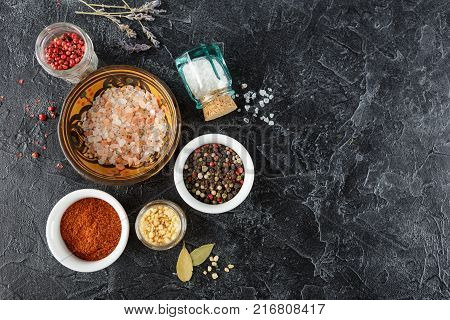 Pink, gold and white salt, black and red peppercorns, bay leaf, paprika on a black background Top view.