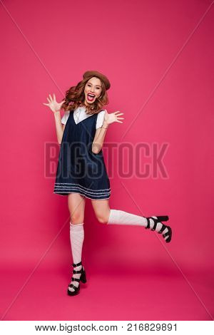 Carfree brunette parisian lady in hat jumping and smiling to camera isolated over pink