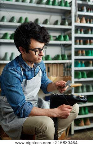 Cobbler with handtool taking out nails from shoe sole while repairing it