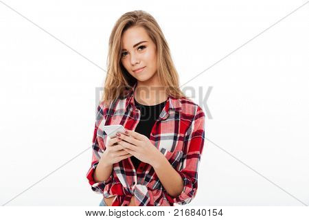 Portrait of a lovely sweet girl in plaid shirt holding mobile phone and looking at camera isolated over white background