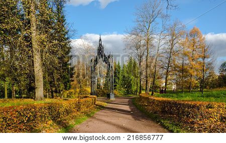 Bright landscape in the autumn Park with iron Gothic gate on blue sky background
