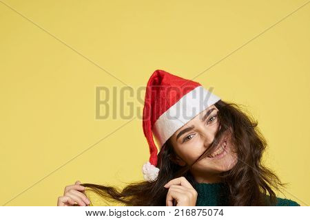 beautiful woman in a New Year hat holds her hair with her hands, light yellow background, free space for copying.