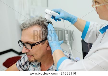a man with gray hair at the reception at the dermatologist. the doctor examines the patient's hair using a method trihoskopii