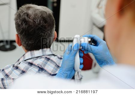a man with gray hair at the reception at the dermatologist. the doctor examines the patient's hair using a method trihoskopii