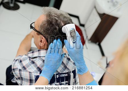 a man with gray hair at the reception at the dermatologist. the doctor examines the patient's hair using a method trihoskopii