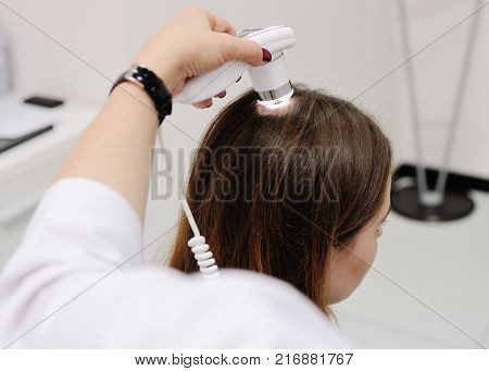 Doctor examines the hairy part of the patient's head - pretty young girl. Trihoskopiya, psoriasis, dandruff, split ends, peeling, dermatology.