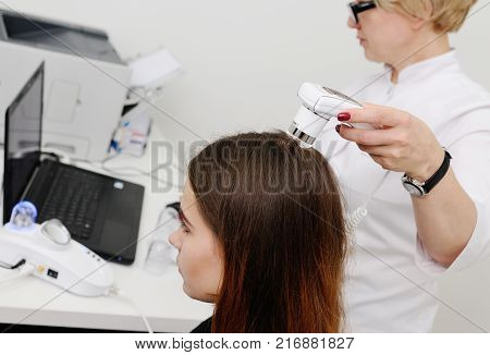 Doctor examines the hairy part of the patient's head - pretty young girl. Trihoskopiya, psoriasis, dandruff, split ends, peeling, dermatology.