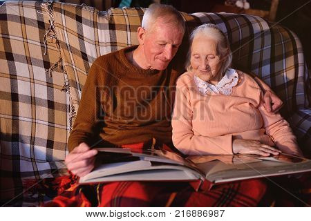 An elderly couple is considering a family photo album wrapped up in a plaid. Golden wedding, happy marriage, grow old together