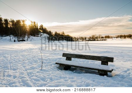 Wooden bench close to a frozen lake in Bogstadvannet Oslo. Winter low sun