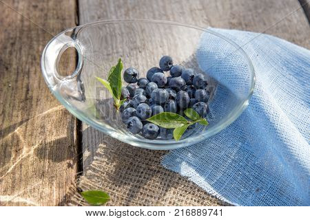 Fresh forest berry, blueberries in a glass plate on a wooden table.