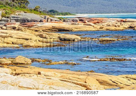 Blue water and red rocks coloured by lichen - Bicheno Tasmania, Australia