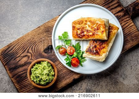 Mexican chimichanga on white plate served with guacamole sauce. Fried tortilla stuffed with chicken and vegetables. Traditional Mexican food, Top view.