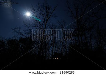 Silhouette of house and forest with full moon overhead at night