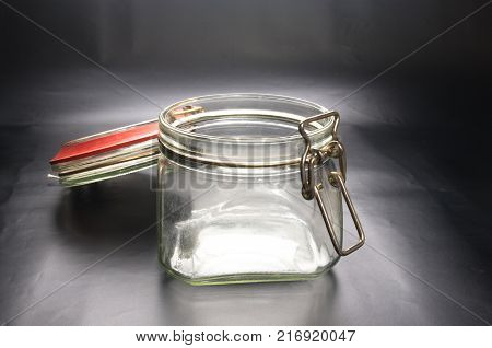 Empty glass jar with the open cap hold with metal wire over the black background