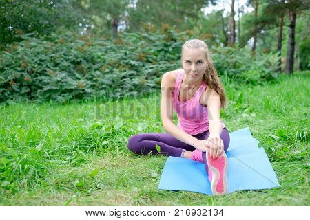 Beautiful sport woman doing stretching fitness exercise in city park at green grass.