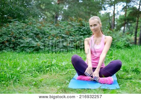 Beautiful sport woman doing stretching fitness exercise in city park at green grass.