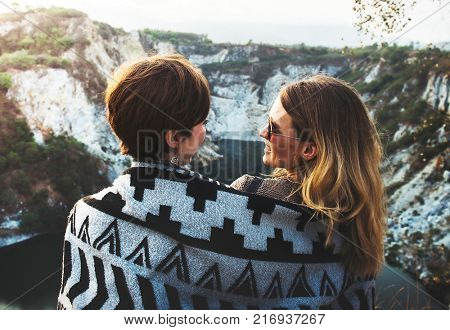 Girlfriends cuddle together under blanket on top of the mountain