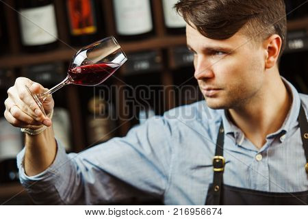 Bokal of red wine on background of male sommelier appreciating color, quality, flavor and sediments of drink. Professional degustation expert in winemaking.