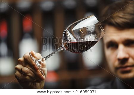 Bokal of red wine on background of male sommelier appreciating color, quality, flavor and sediments of drink. Professional degustation expert in winemaking.