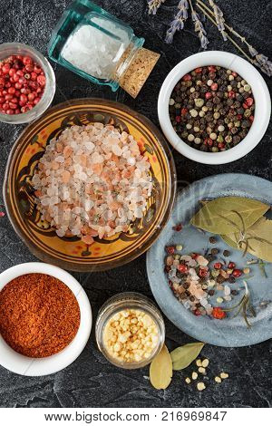 Pink, gold and white salt, black and red peppercorns, bay leaf, paprika on a black background Top view.