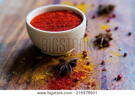 Close up white wooden bowl filled with paprika powder on dark wooden surface covered with anise and turmeric