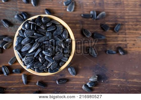 Close up unpeeled sunflower seeds in wooden bowl on dark wooden table