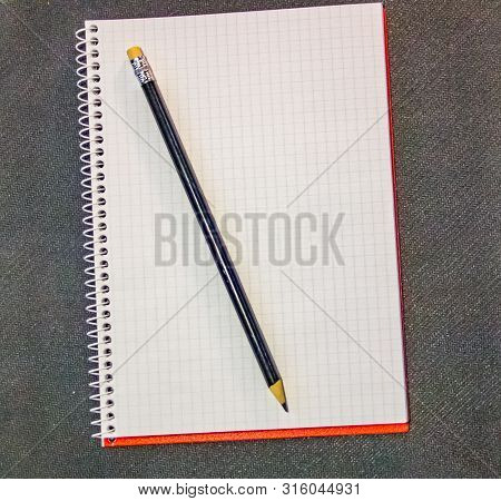 Design Concept - Top View Of A Red And Gray Spiral Notebook And Black Pencil Collection On Black Bac