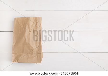 Paper Bag On Wooden White Background With Empty Space For Text. Flat Lay, Top View.
