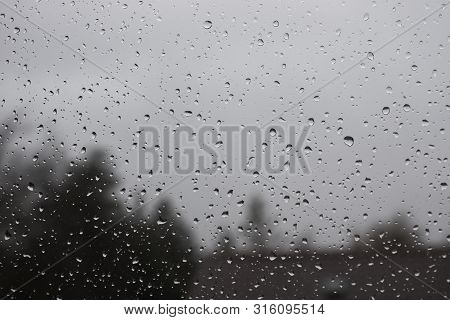 Water Drops On Window With Blurred Trees And House In Background.
