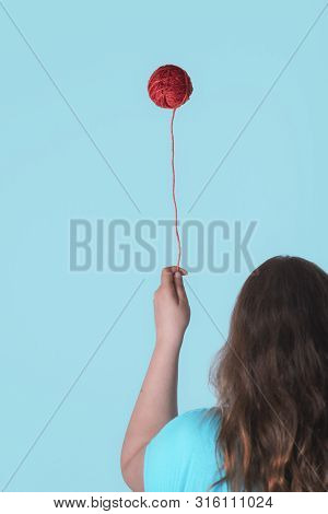 Strange Childhood Concept With A Woman Holding A Floating Red Thread Ball Like A Balloon. Weird Knit