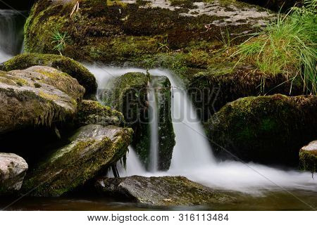 Long Exposure Of A Small Watefall Flowing Over Mossy Rocks In A Freshwater River