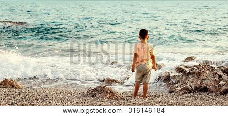 Little Boy Playing On A Rocky Beach With Crystal Turquoise Water Of Ionian Sea In Albania. Calm And 