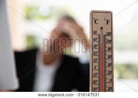 Thermometer In Front Of Businessman Working During Hot Weather In The Office