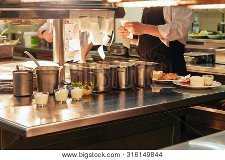 Food Orders On The Kitchen Table In The Restaurant, Chief Reading Orders And Cooking In Professional