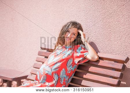 The Pregnant Girl Basks In The Sun. The Concept Of Warm Leisure - A Beautiful Pregnant Girl With Lon